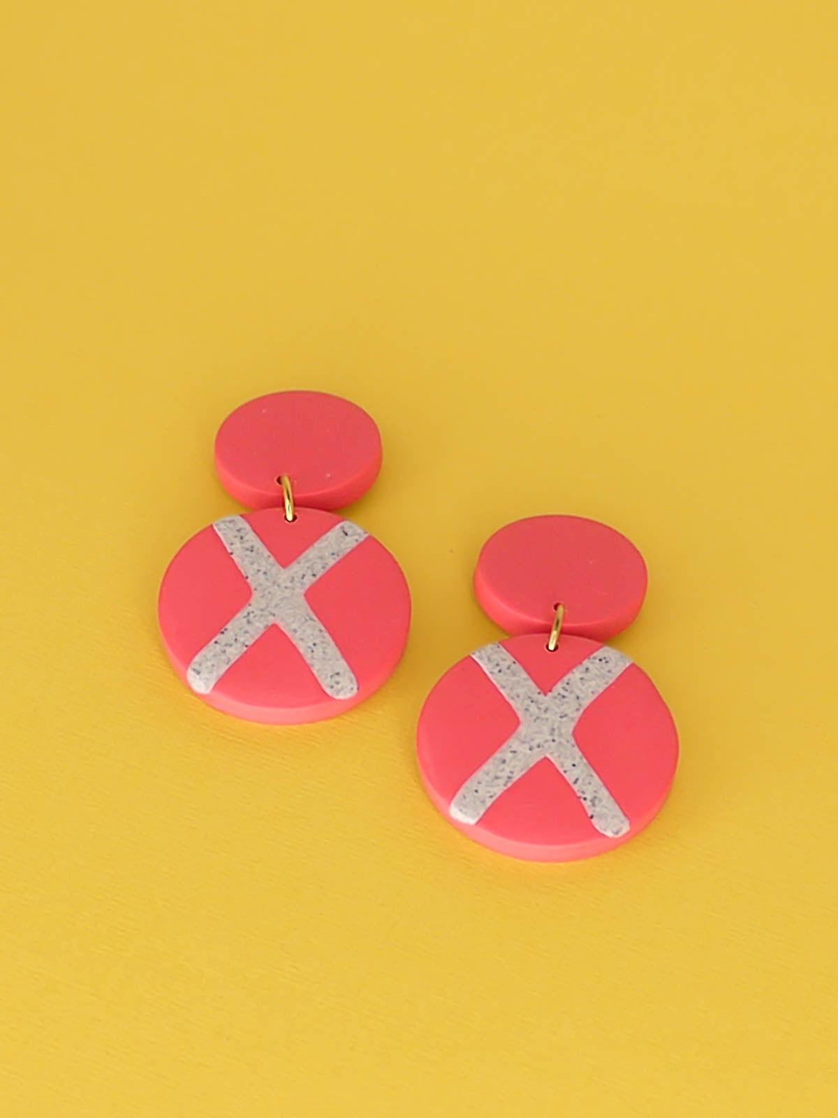 Polymer clay dangle statement earrings with a pink stud connected to a pink circle with a granite cross in the centre