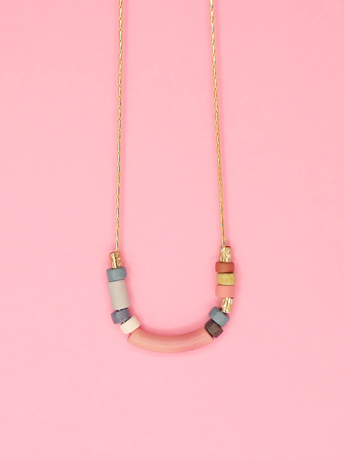 Pink curved bar ceramic bead necklace with colourful ceramic tube and brass beads strung on a gold plated thin chain with clasp