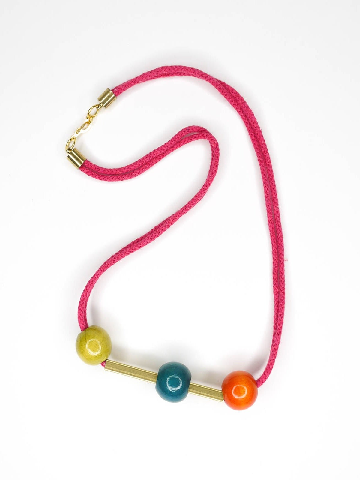 Geometric statement necklace in hot pink cotton rope with a brass bar in the centre with contrasting wooden beads on either side in orange and green and a turquoise bead over the brass bar with a brass clasp