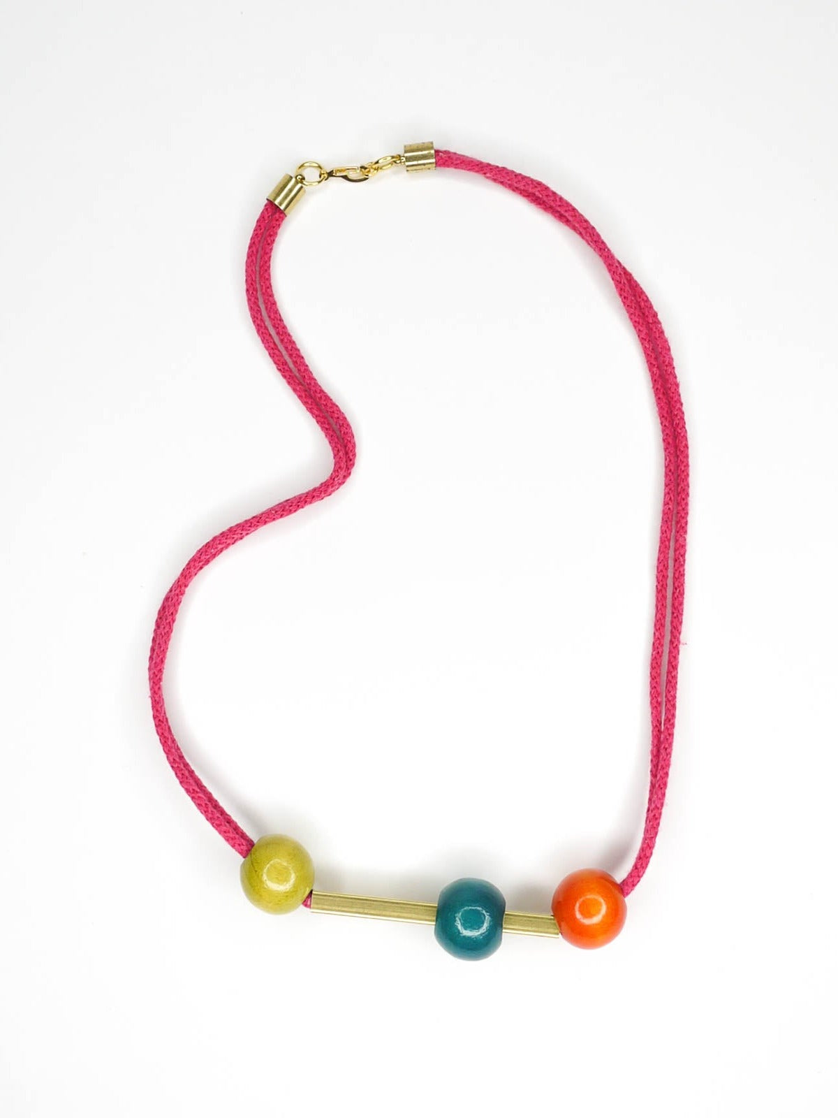 Geometric statement necklace in hot pink cotton rope with a brass bar in the centre with contrasting wooden beads on either side in orange and green and a turquoise bead over the brass bar with a brass clasp