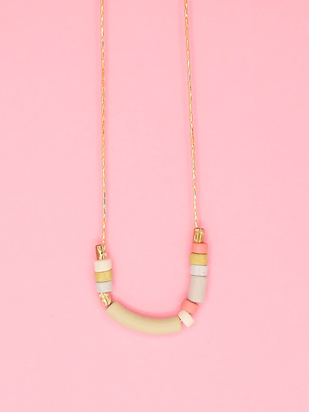 Delicate ceramic beaded necklace with a curved bar pistachio bead and multicoloured tube and brass beads strung on a gold plated snake chain