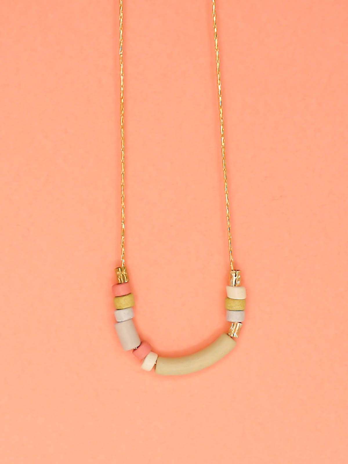 Delicate ceramic beaded necklace with a curved bar pistachio bead and multicoloured tube and brass beads strung on a gold plated snake chain