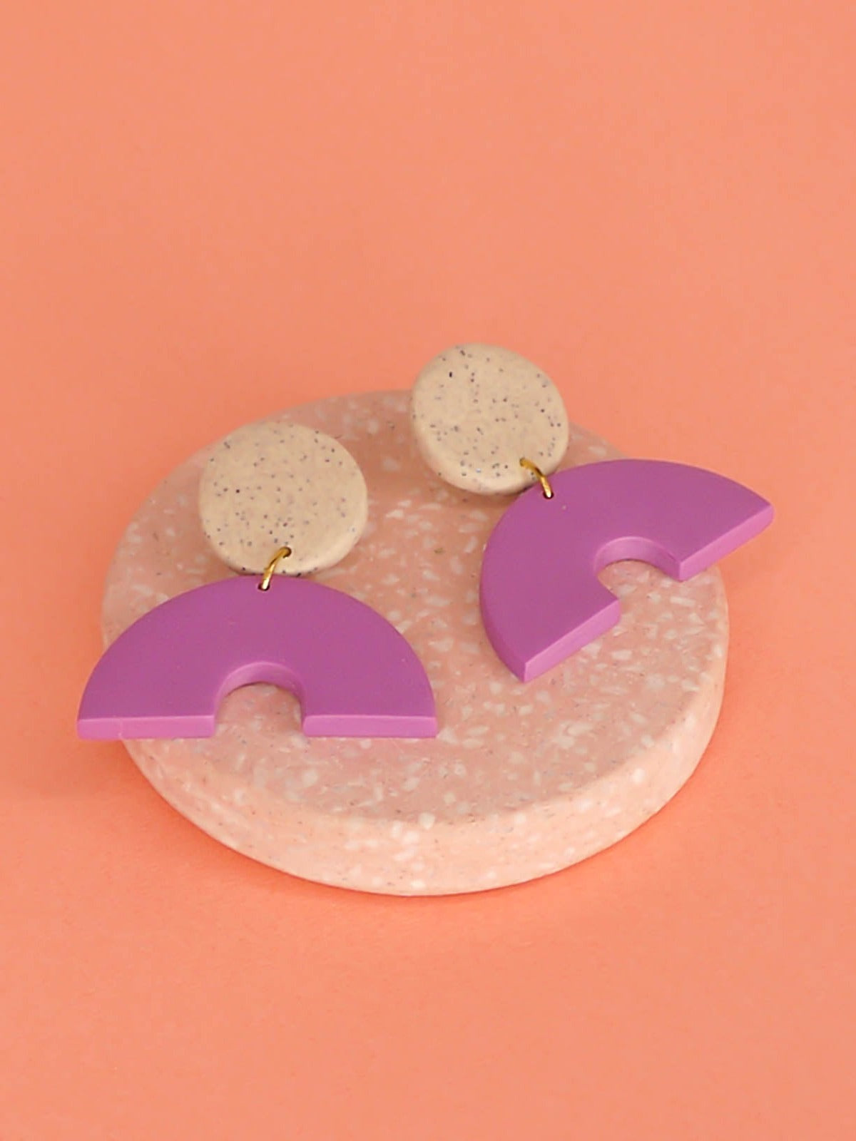 Geometric arch dangle earrings with a purple arch connected to a granite stud with stainless steel posts, made out of lightweight polymer clay