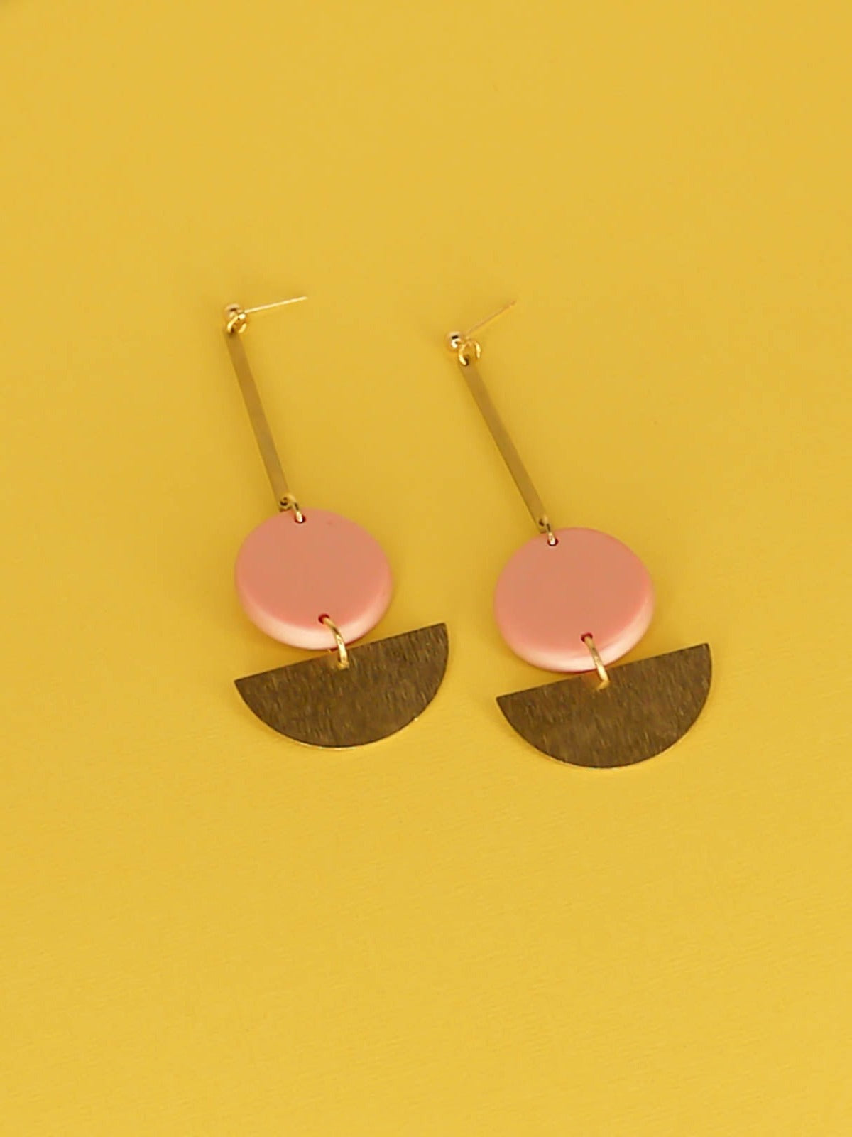 Dangle geometric statement earrings with a gold plated ball stud, a brass stick with a polymer clay round metallic circle in rose gold connected to a textured brass semi circle