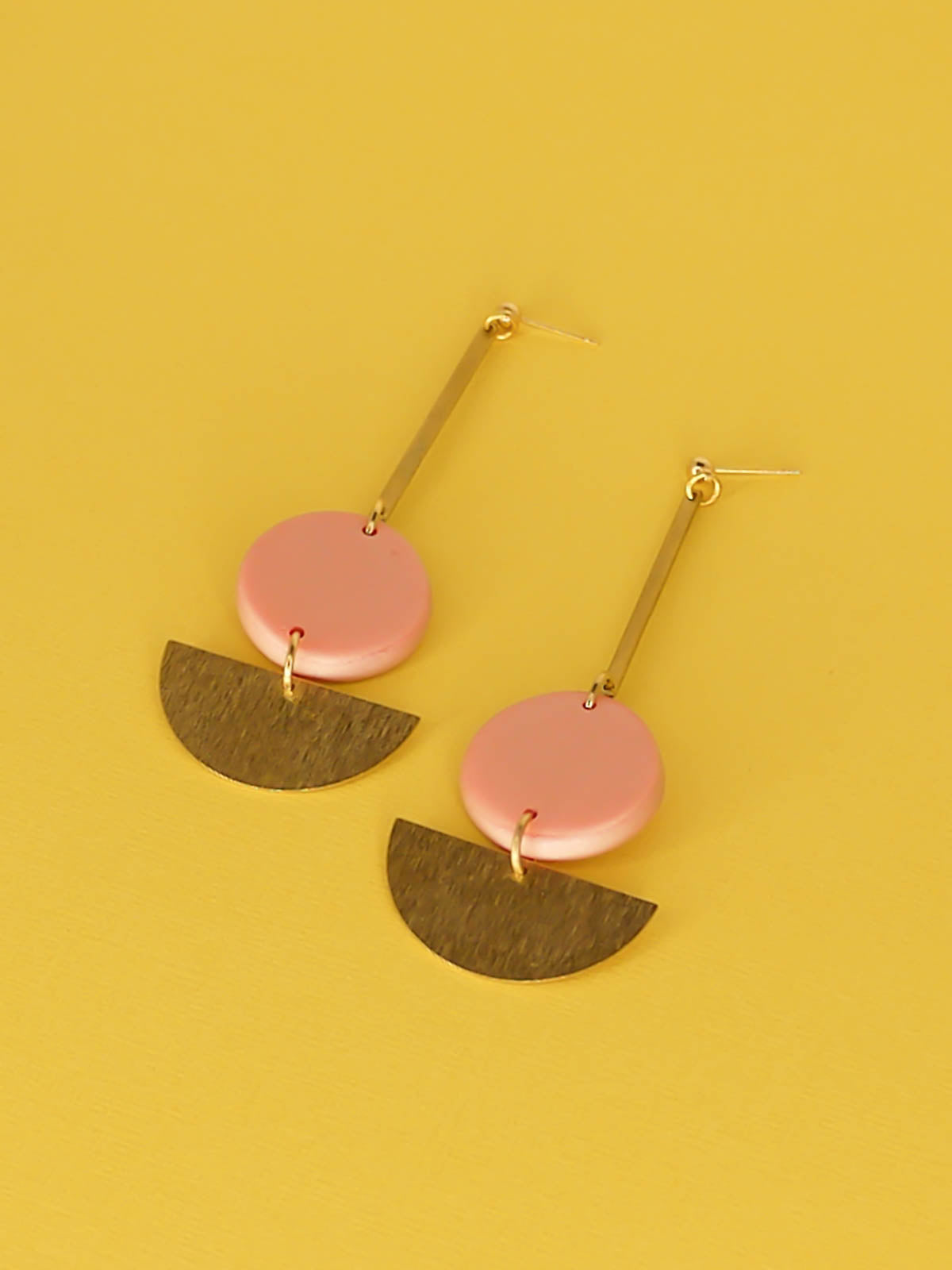 Dangle geometric statement earrings with a gold plated ball stud, a brass stick with a polymer clay round metallic circle in rose gold connected to a textured brass semi circle