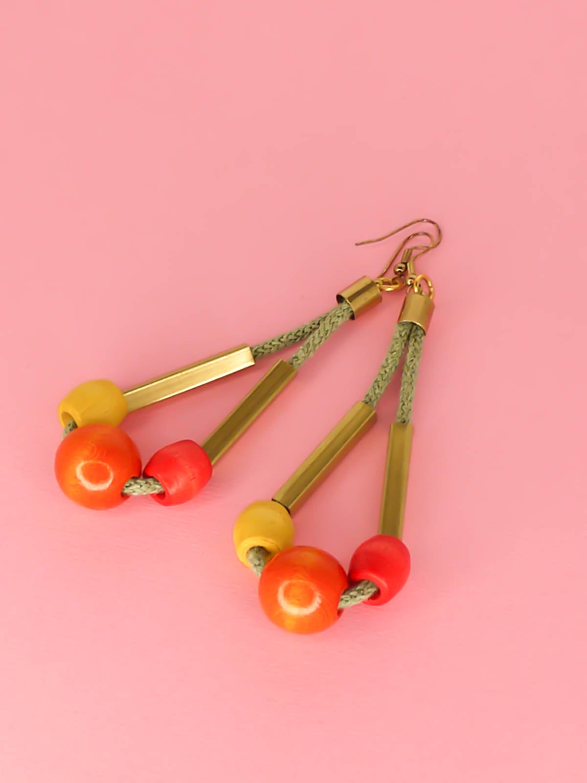 Long bead dangle statement earrings with wooden beads in watermelon, orange & green & brass tube beads strung on mustard coloured cotton rope with brass end caps, hung from gold plated brass earring hooks.