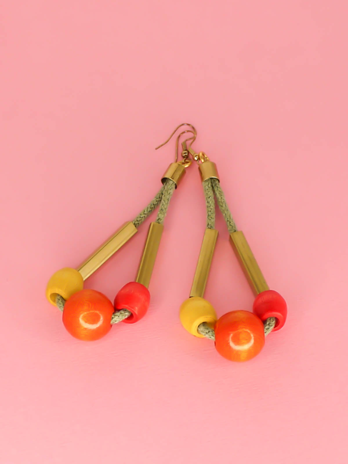 Long bead dangle statement earrings with wooden beads in watermelon, orange & green & brass tube beads strung on mustard coloured cotton rope with brass end caps, hung from gold plated brass earring hooks.