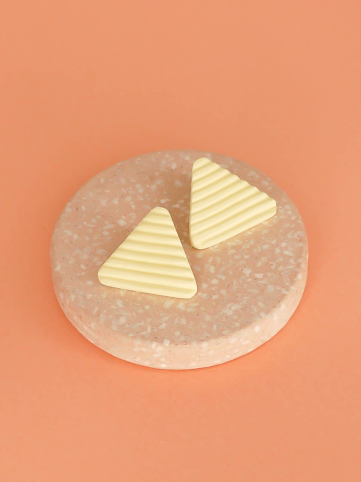 Lightweight yellow polymer clay triangle stud earrings in a fluted striped texture with stainless steel studs.